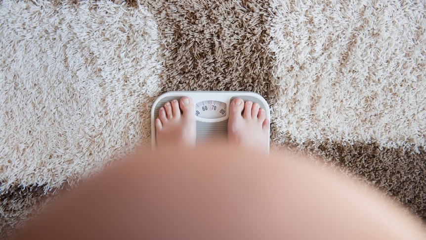 A pregnant woman stands on a pair of scales.