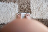 A pregnant woman stands on a pair of scales.