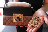 A designer bag and rings up held in a staffer's hand up for public auction after being left at Brisbane airport.