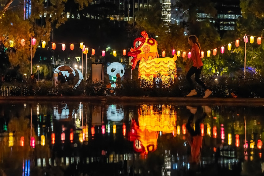 A child runs by a body of water. Behind her are large lantern sculptures, including of a panda and a yellow dragon