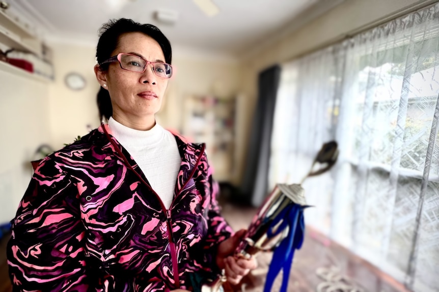 A woman stands in her empty house with a trophy