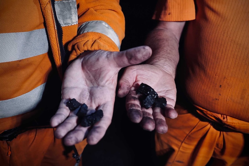 Men in high vis gear holding lumps of coal