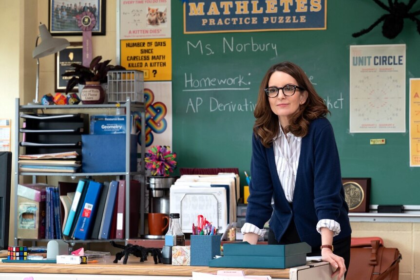 Tina Fey leans over a desk in a classroom.