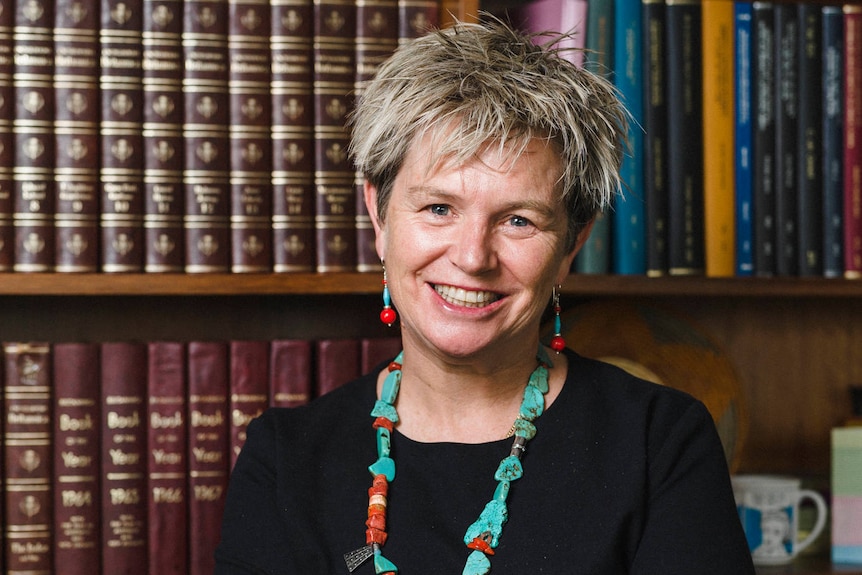 Woman in front of bookcase crosses arms and smiles.