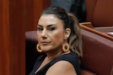 Thorpe sits at a senate bench looking towards the camera, an Aboriginal flag tattoo visible on her arm.