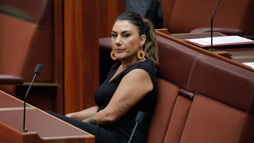 Thorpe sits at a senate bench looking towards the camera, an Aboriginal flag tattoo visible on her arm.