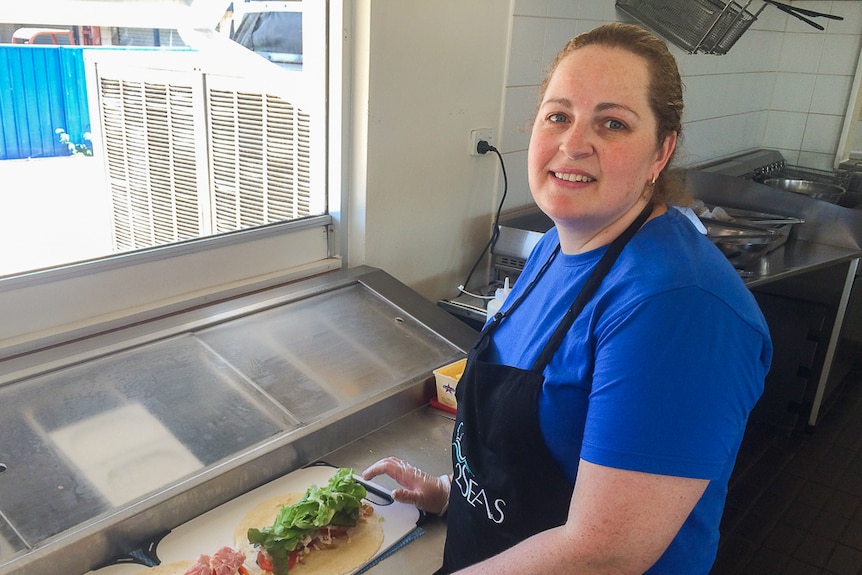 A woman with dark blonde hair in a blue shirt prepares wraps with salad and ham on them.