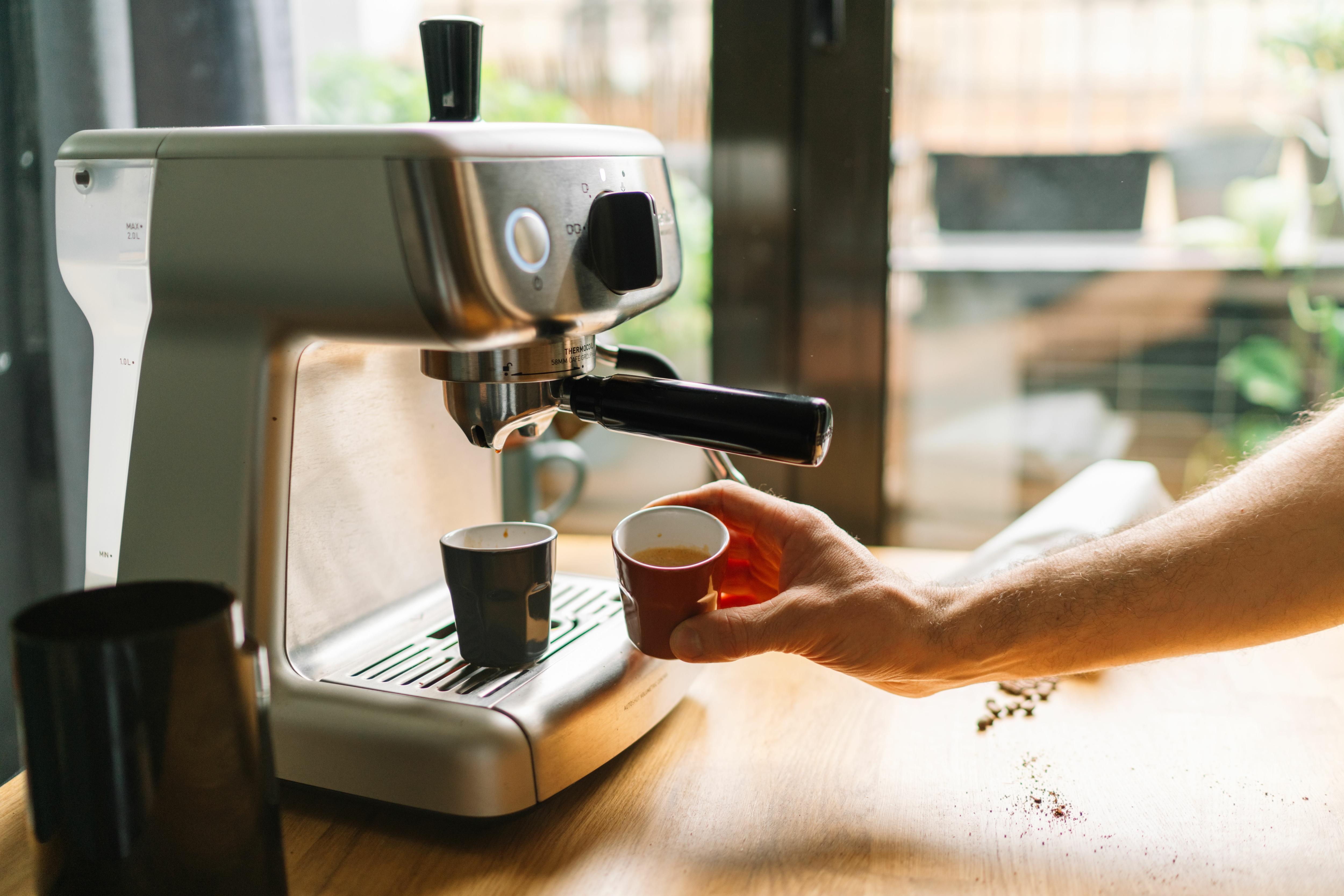 A person making coffee with an espresso machine in a cozy kitchen setting.