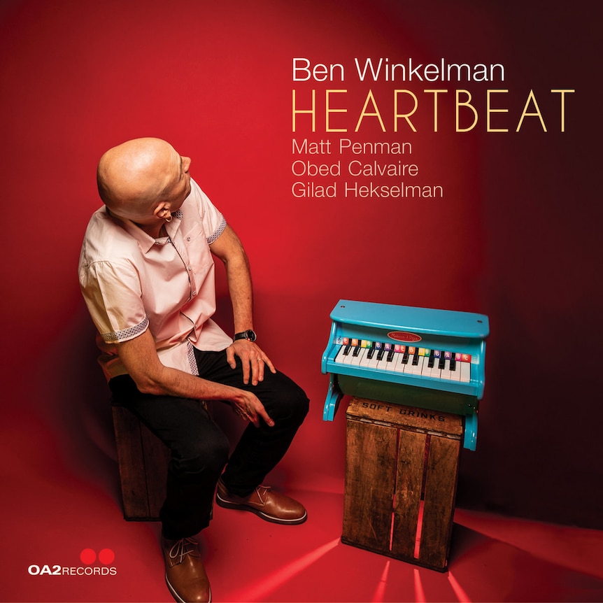 Ben Winkelman sits is a red room with a small, blue piano; he's looking behind him