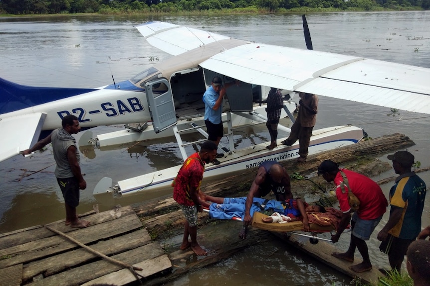 Several men help an injured person in a stretcher into a seaplane.