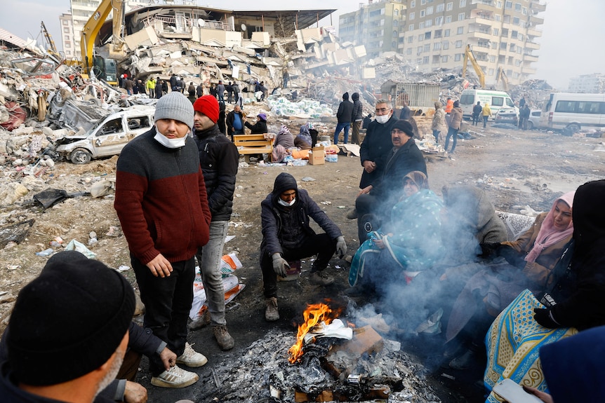 People sit next to the fire at the site of a collapsed building in Turkiye.