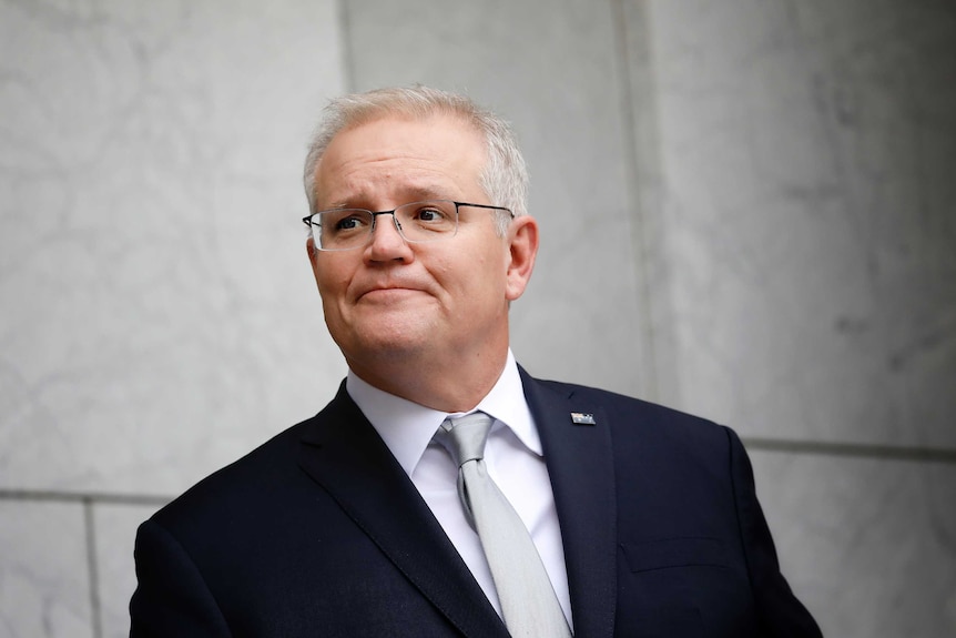 Scott Morrison, wearing a suit and silver tie, purses his lips while standing in a marble-walled courtyard