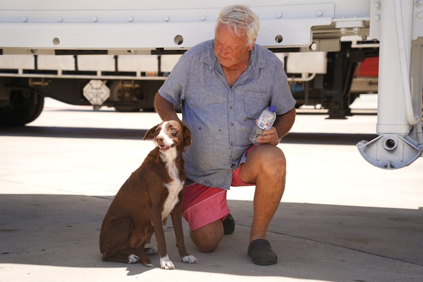 Barry kneeling on one knee in front of his truck. Floss sits next to him. 