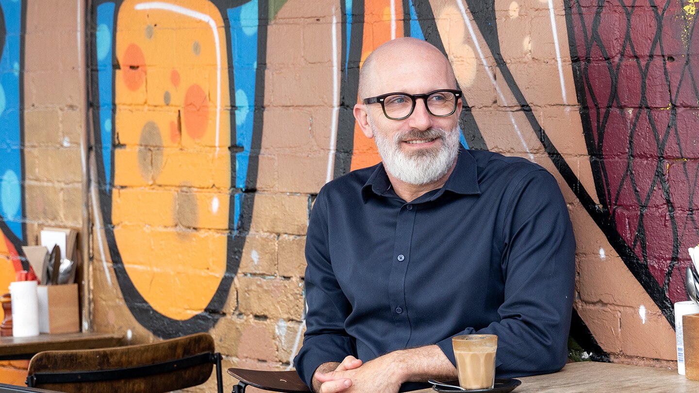 Man sits with back against wall smiling