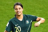 Sam Kerr holds her captain's armband in her right hand, smiling.