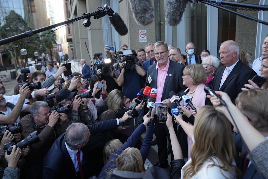 A man speaks to a large number of reporters