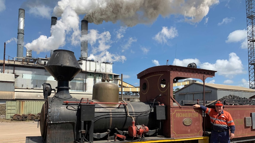 A man stands in front of a steam engine at a railway station