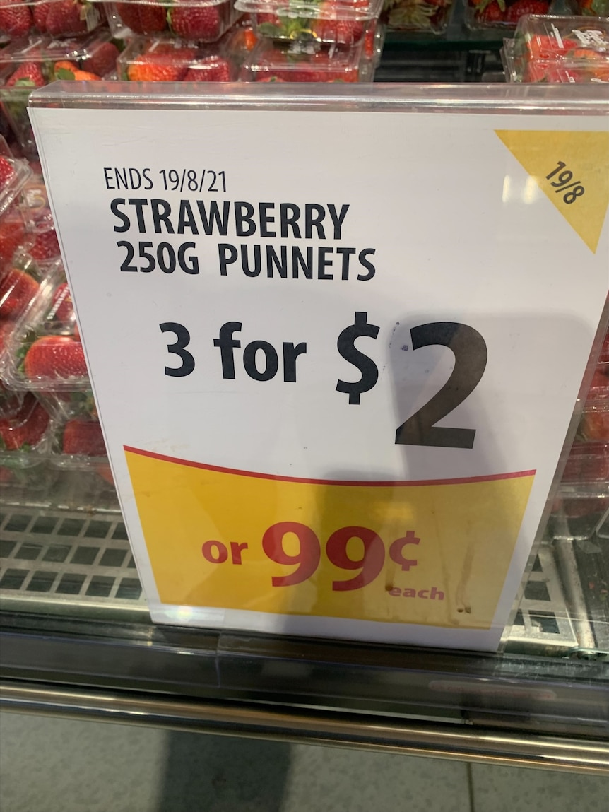 A "3 for $2" sign in front of punnets of strawberries.