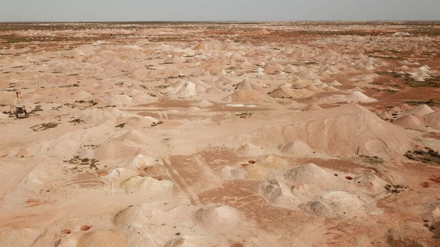 Mounds of dirt cover vast tracks of flat desert red sand across the horizon