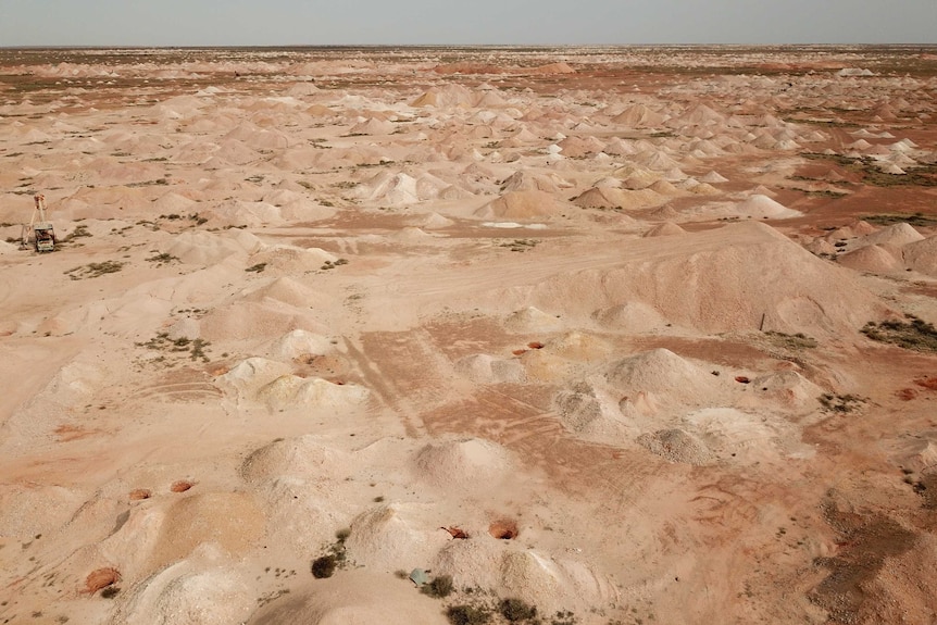 Mounds of dirt cover vast tracks of flat desert red sand across the horizon