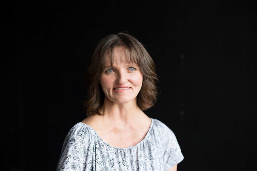 Tracey Morris pictured smiling against a black background to depict a story on how to spot domestic violence and what to do.