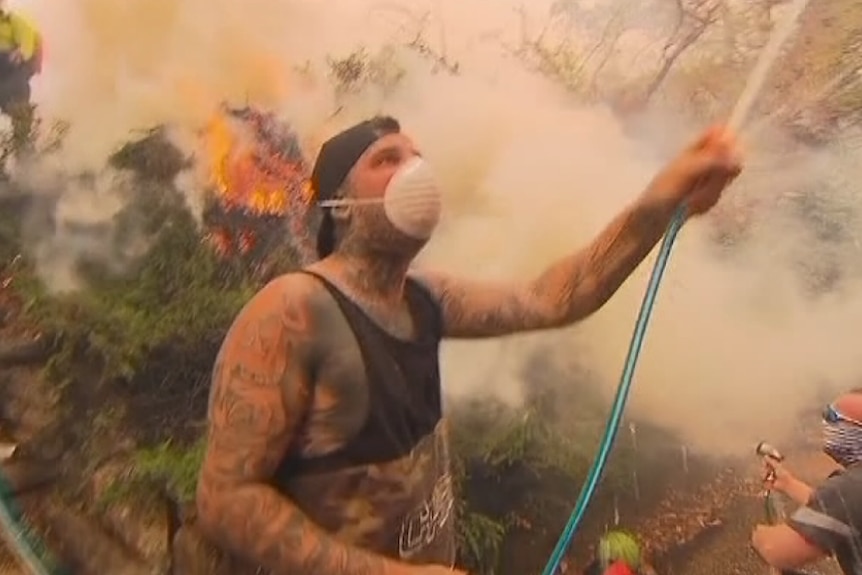 A man wearing a disposable dust mask hoses down a house in Menai in southern Sydney to defend it from bushfire.