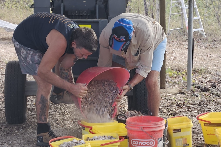 Two men pouring dirt into buckets.