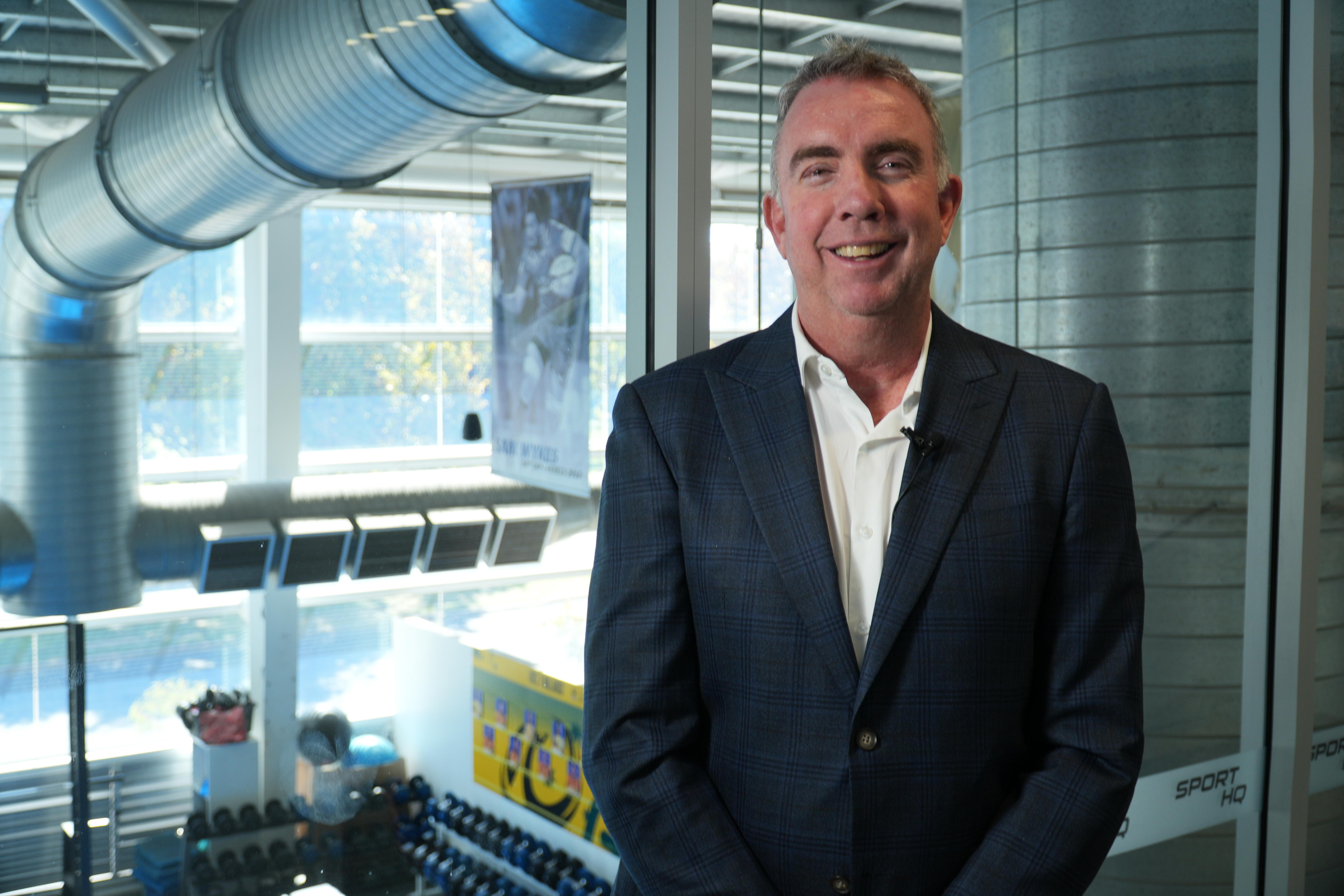 Troy Kirkham stands indoors smiling. 