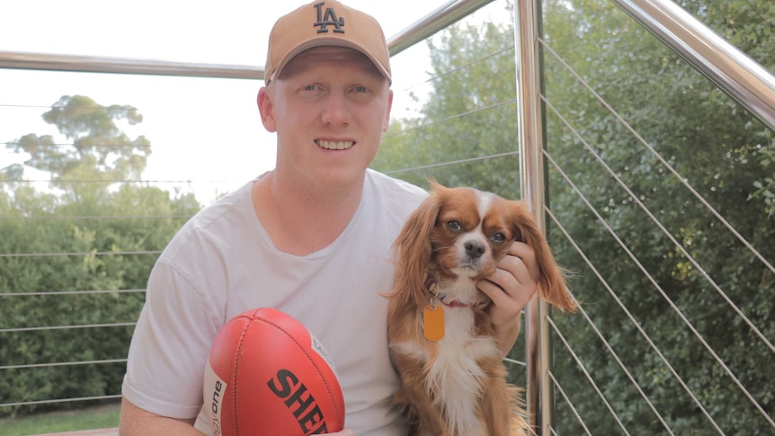 Former Essendon and Brisbane footballer Josh Green sits on stairs with a football and a dog.