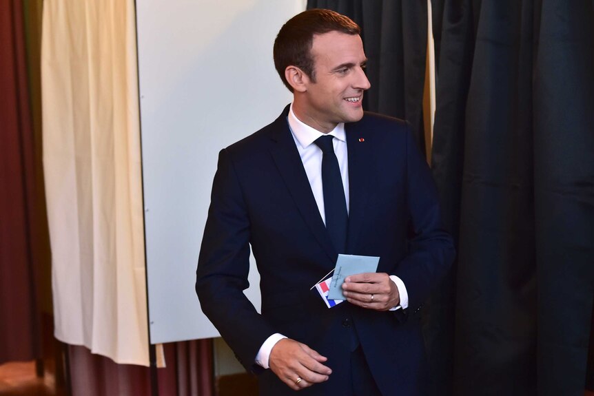 Emmanuel Macron exits a pooling booth with voting papers in his hand.