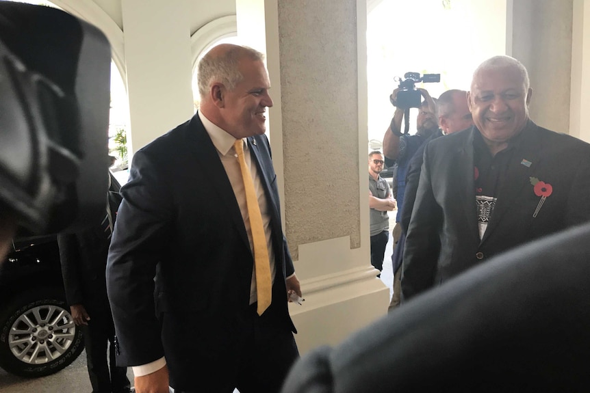 Scott Morrison is greeted by Fiji's Prime Minister Frank Bainimarama in Suva, Fiji. They are being filmed by journalists.