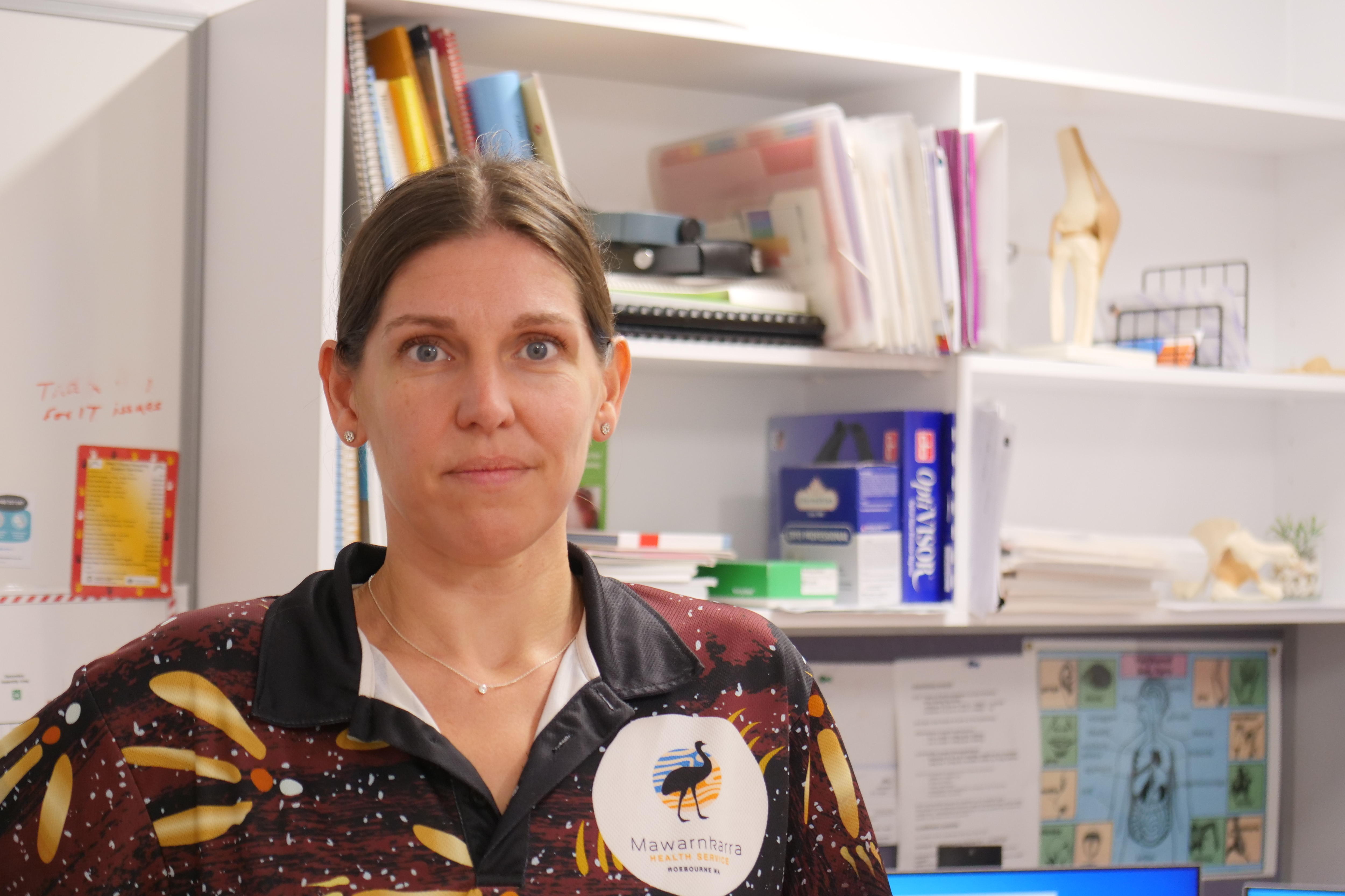 A woman with brown hair smiles at the camera in an office with books on a shelf in the background.