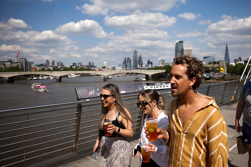 People walk across a bridge with drinks in hand.