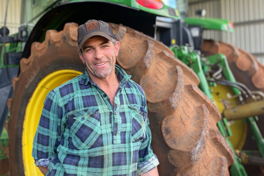 A farmer stands behind of a tractor that is parked in shed.