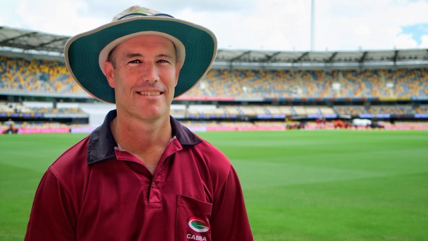 A man wearing a hat and a maroon polo shirt with the "Gabba" logo on the pocket smiles as he stands on the grass.