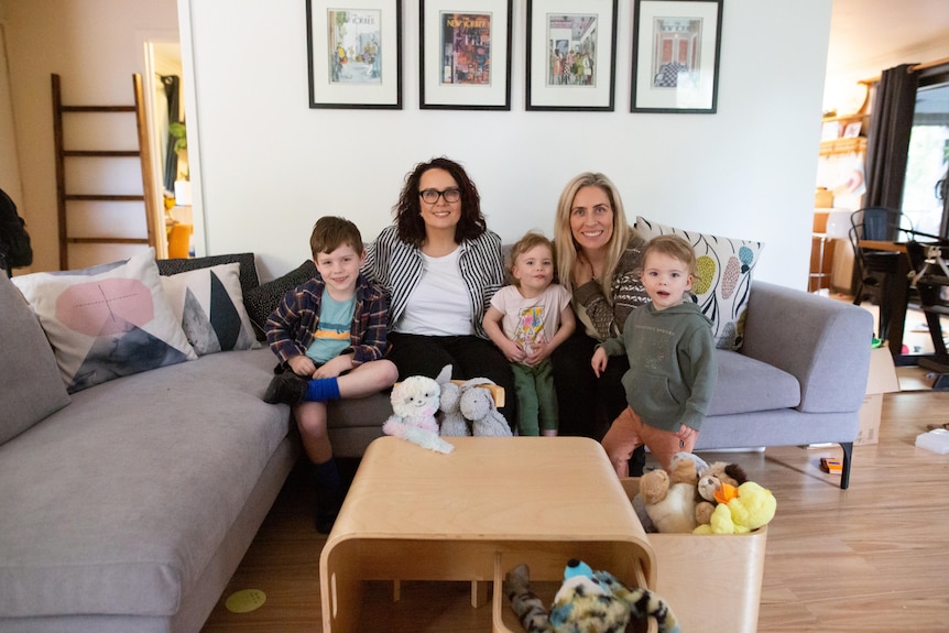 Bec and Sharon sit on the couch with their three children.