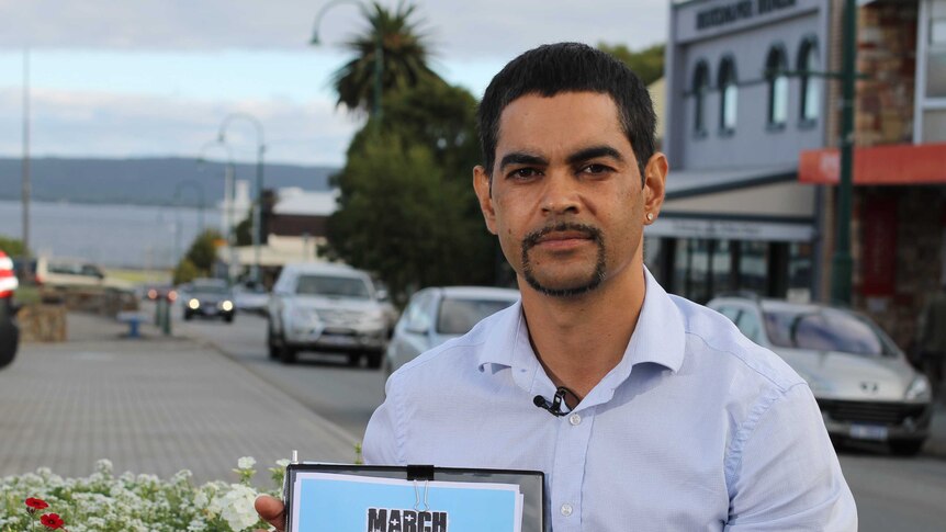 Aboriginal youth worker, Stuart Roberts, sits in Albany's main street, holding sign advertising the March Against Meth