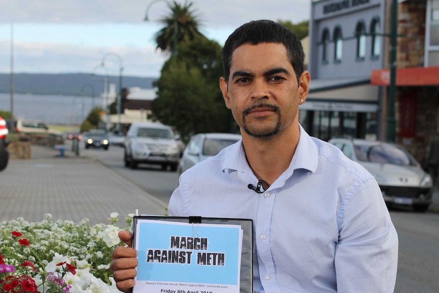Aboriginal youth worker, Stuart Roberts, sits in Albany's main street, holding sign advertising the March Against Meth