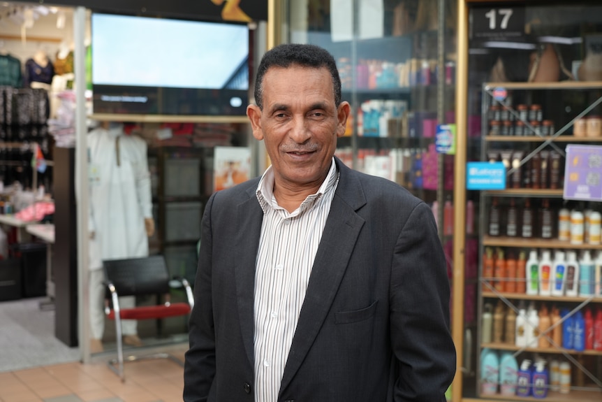 Man wearing a striped white business shirt and dark grey jacket, standing in a shop.