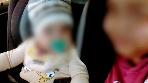 A baby and a young woman in a car. Both have their faces blurred.