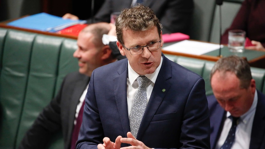 Tudge has hands raised at hip level looking at the Speaker, wearing a blue suit and glasses.