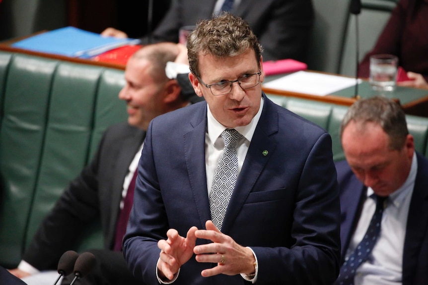 Tudge has hands raised at hip level looking at the Speaker, wearing a blue suit and glasses.
