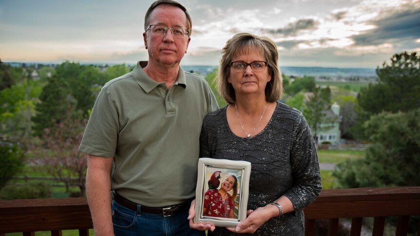 A couple hold a framed photo of a young woman