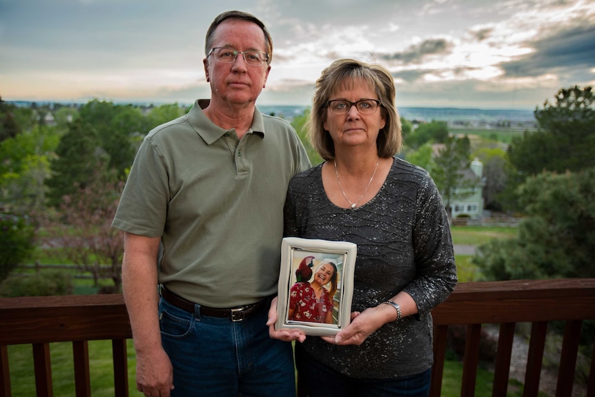 A couple hold a framed photo of a young woman