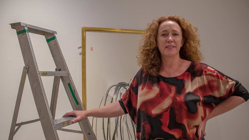A woman standing next to a ladder and an artwork in a gallery space