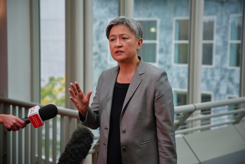 Penny Wong holds up her hand while speaking to the media