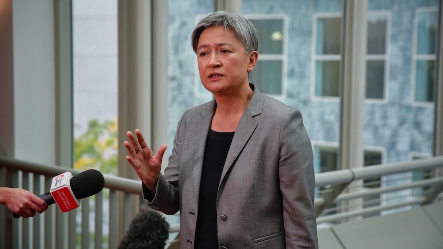 Penny Wong holds up her hand while speaking to the media