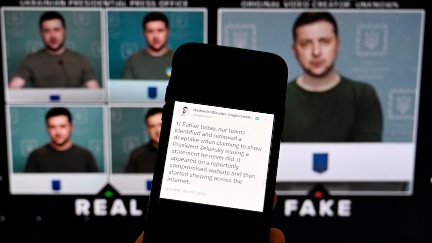 Video screens showing Volodymyr Zelenskyy are behind a phone screen displaying a message about a fake video.