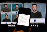 Video screens showing Volodymyr Zelenskyy are behind a phone screen displaying a message about a fake video.