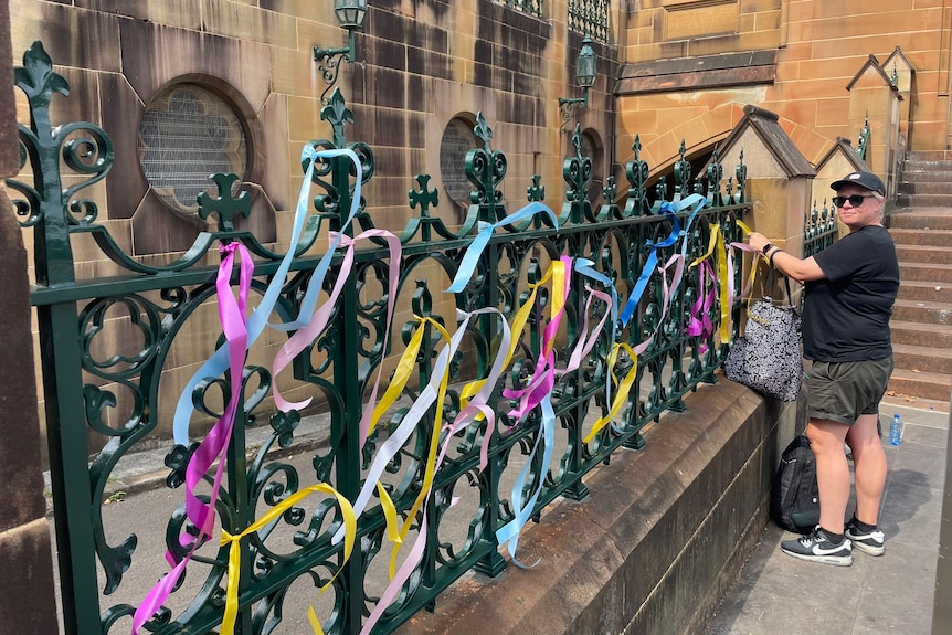 woman ties colourful ribbons to fence of St Marys Cathedral in Sydney